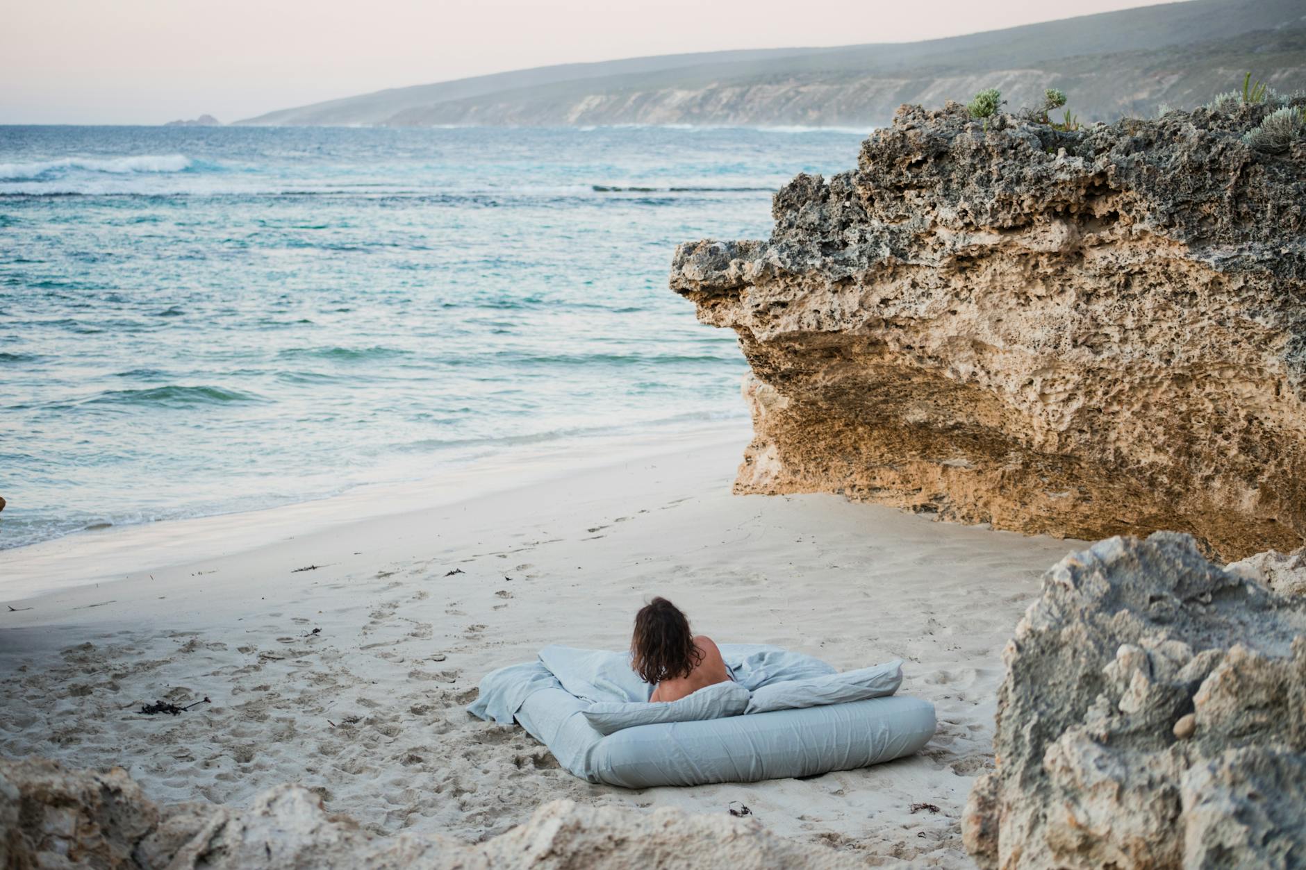 woman lying on a bed on the beach looking at the sea