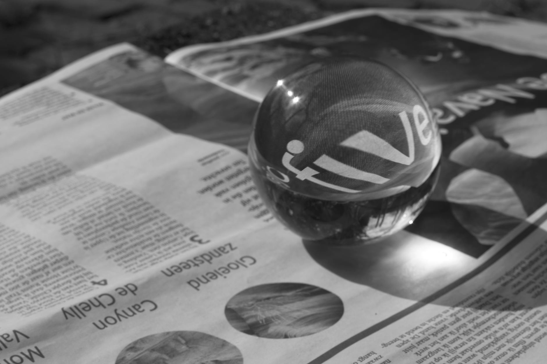 grayscale photography of round clear paper weight on newspaper